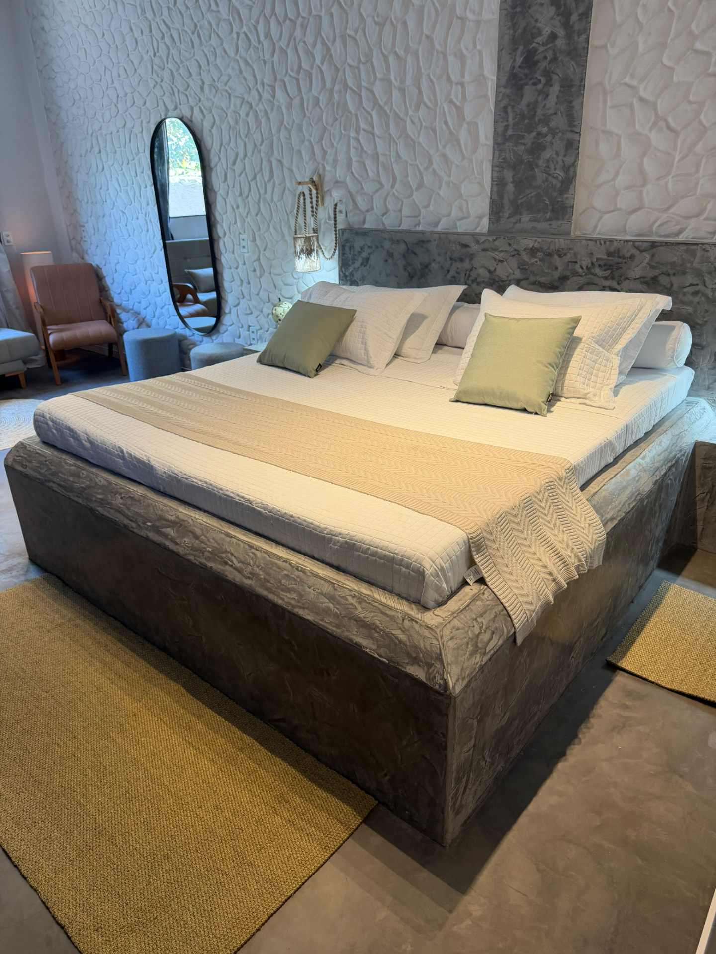 Cama king sobre base de cimento queimado e parede de pedra esculpida