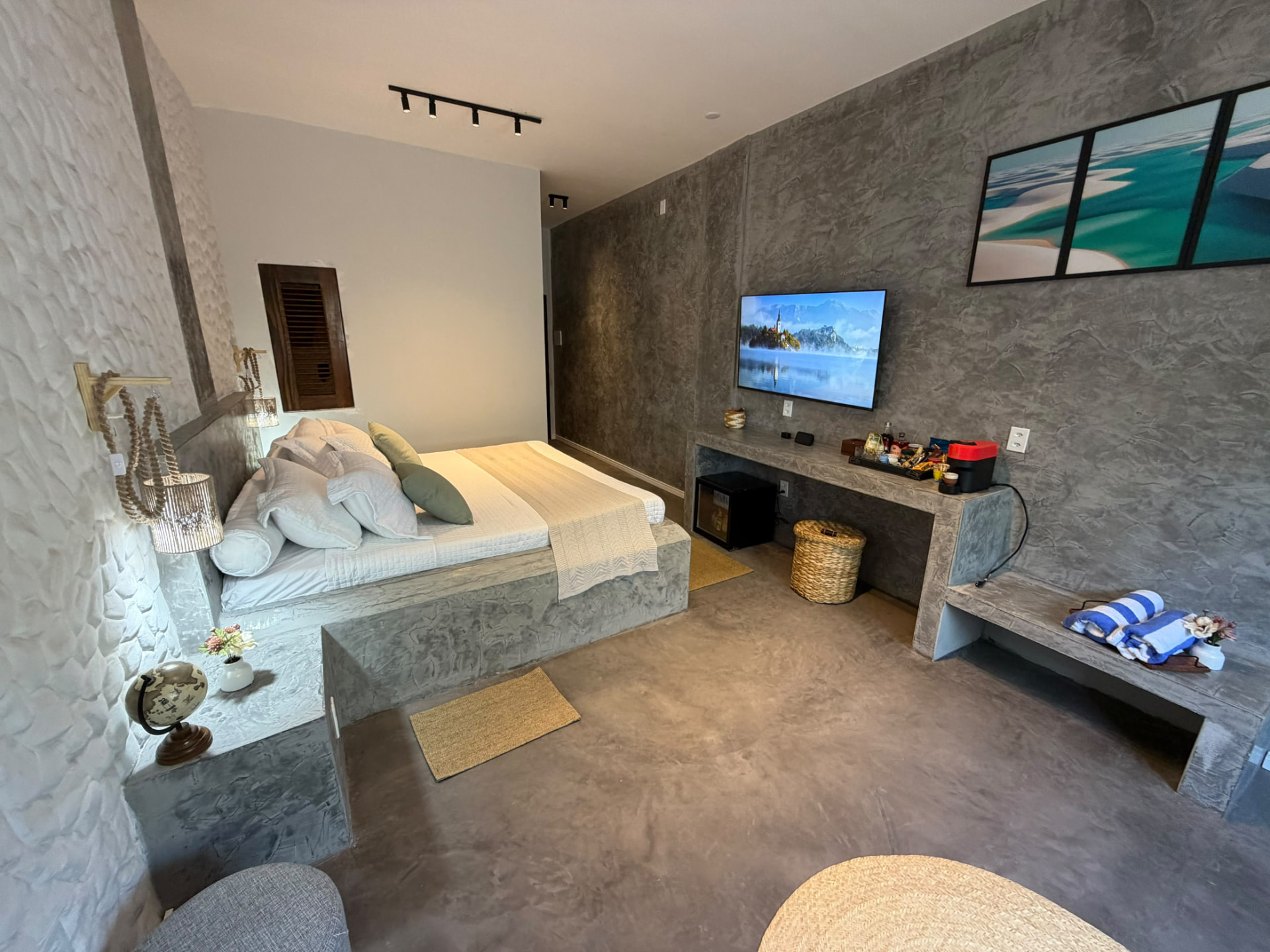Suíte com cama king, TV, bancada em cimento e quadro dos Lençóis