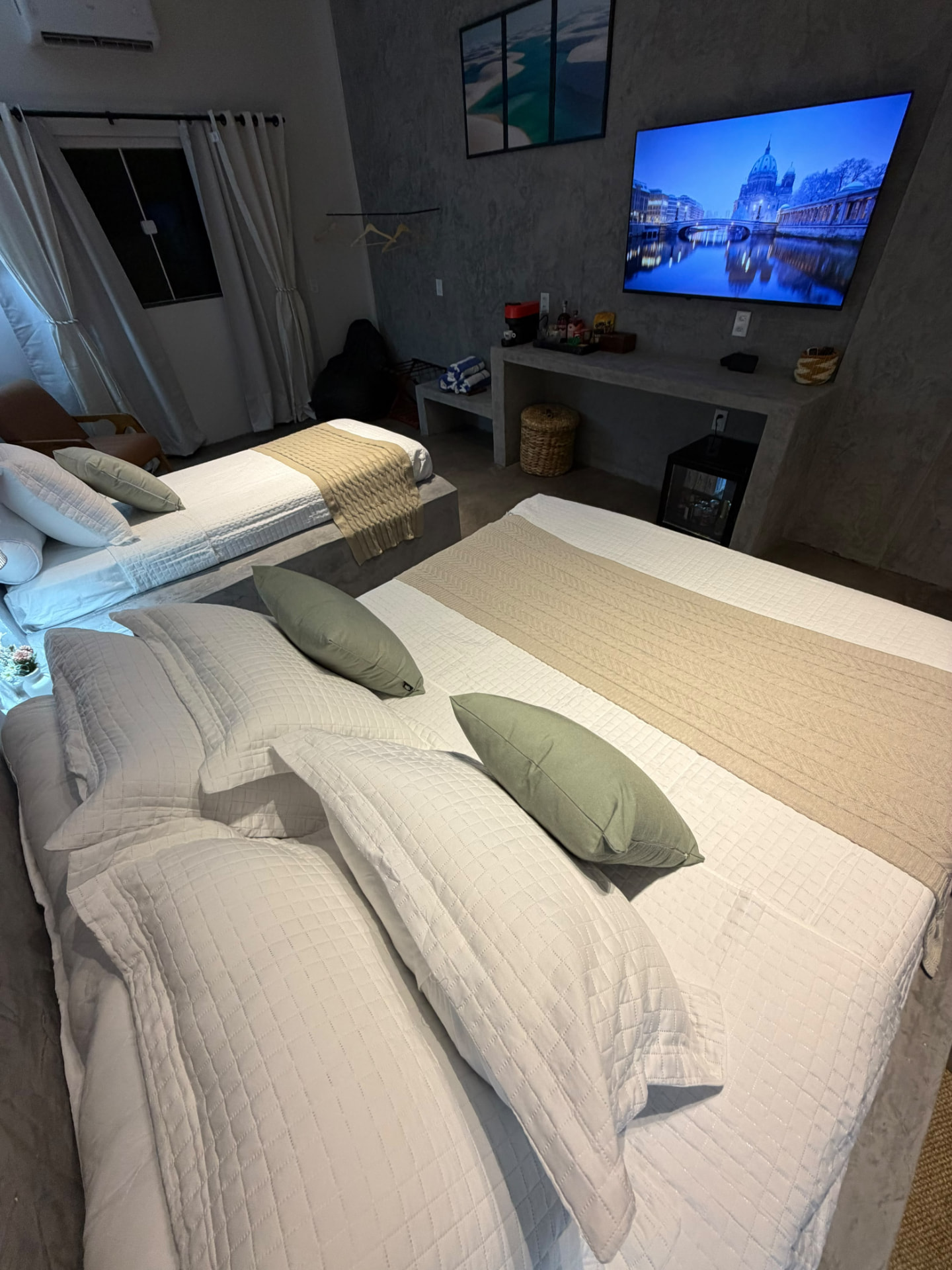 Quarto com cama de casal e solteiro, TV e bancada à noite