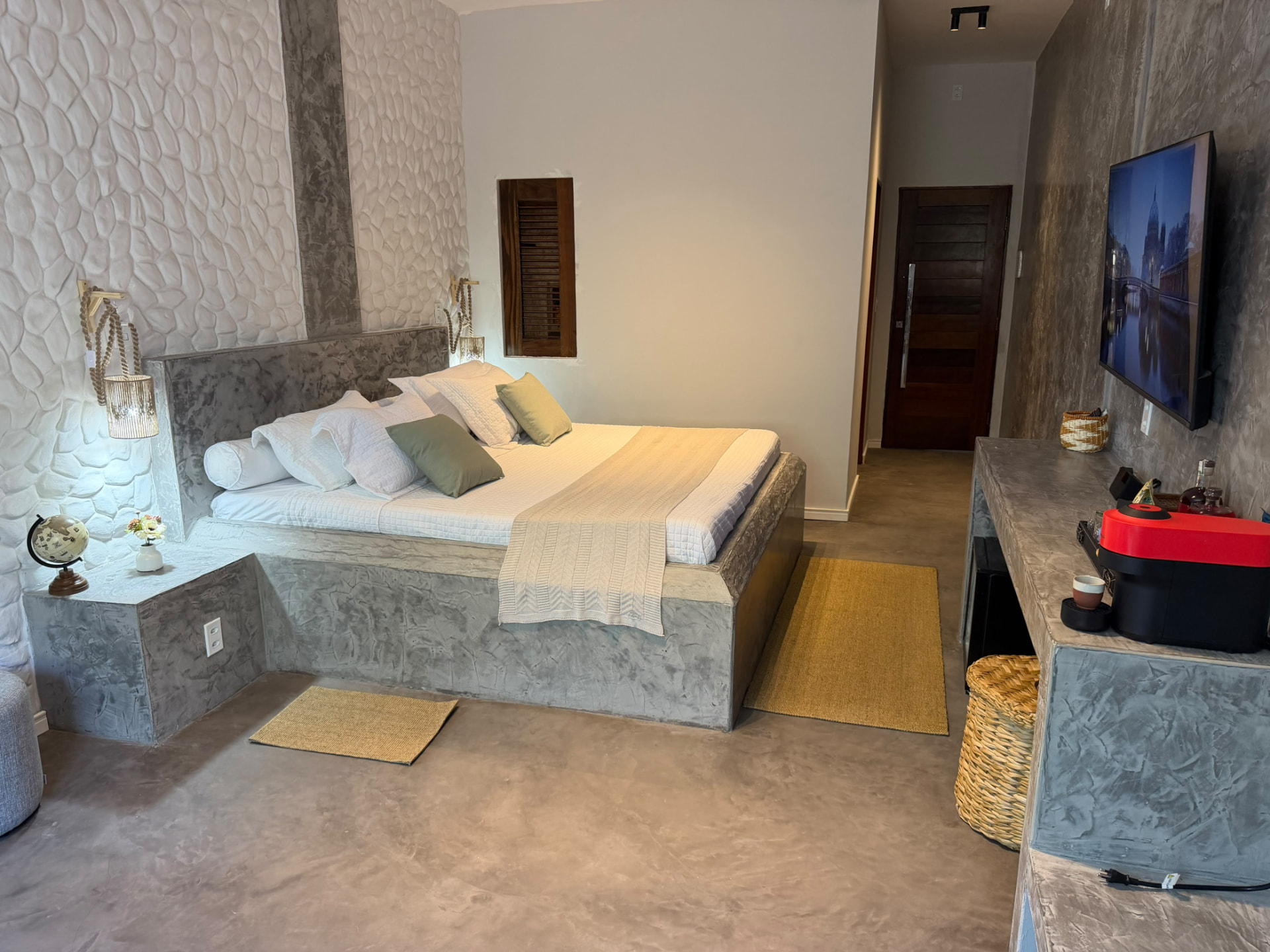 Cama king com arandelas de palha, criado-mudo em cimento e TV